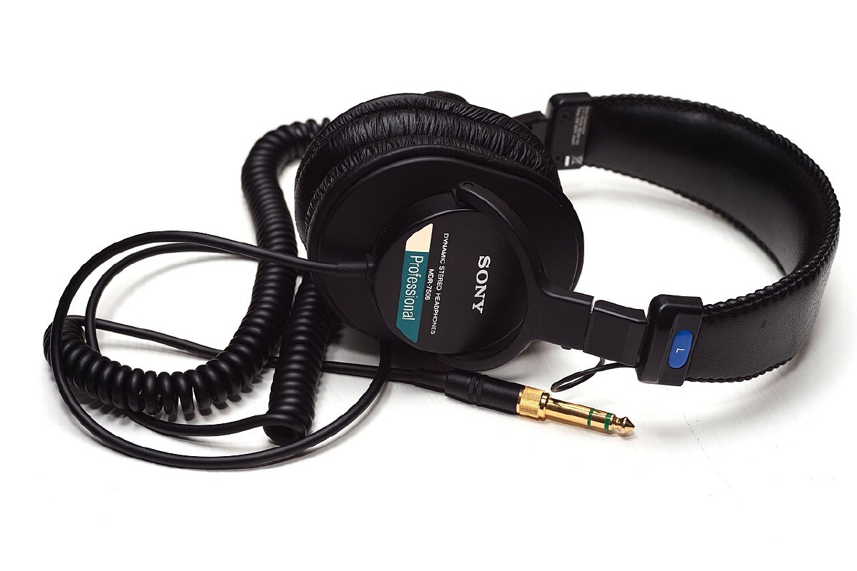 Sony MDR-7506 headphones folded on a white surface, showing the Professional badge, coiled cable, and gold-plated plug